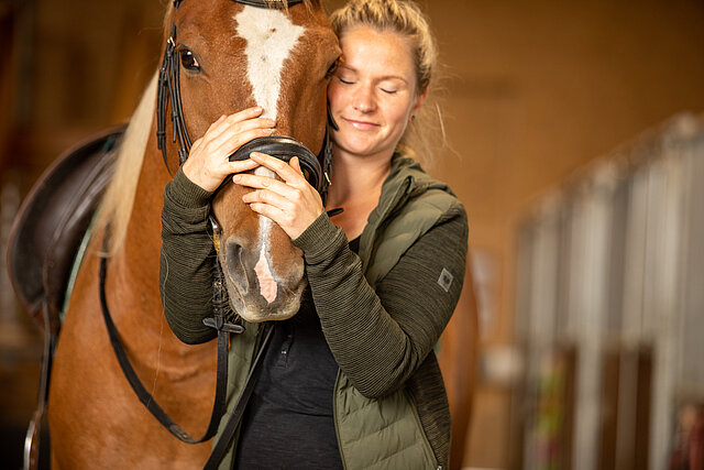 Mitarbeiterin des Ponyhof schmust mit Pferd Kopf an Kopf