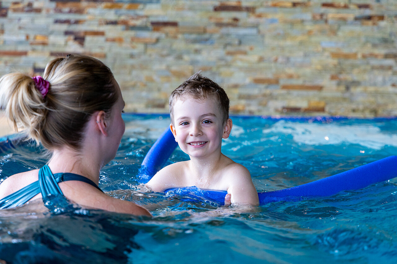 Eine Schwimmlehrerin hilft einem Jungen mit einer Schwimmnudel bei den ersten Schwimmversuchen der Happy Schwimmschule im Elldus Resort.
